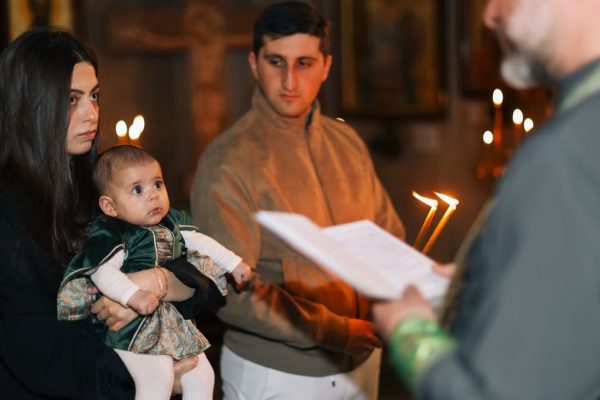 A family participates in a traditional religious ceremony with candlelight indoors.